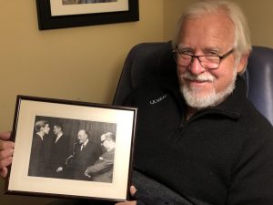 Lars Sandven '69 holds photo of himself standing with King Olav V of Norway who visited Augsburg in 1968.